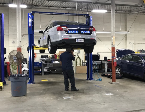 Un empleado revisa un coche de la policía estatal elevado en un ascensor.